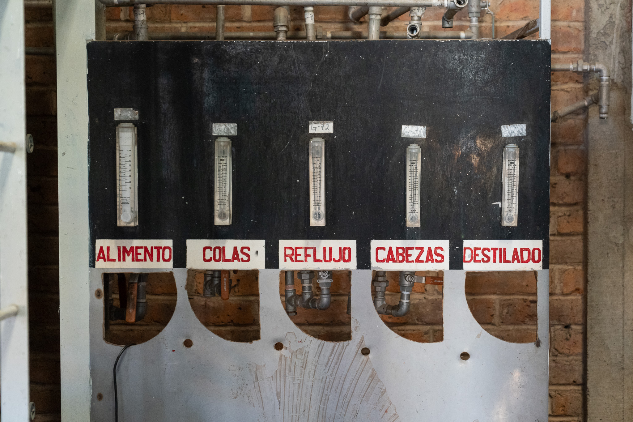 Hand-painted flow gauges on a distillery still panel, labelled alimento, colas, reflujo, cabezas, destilado.